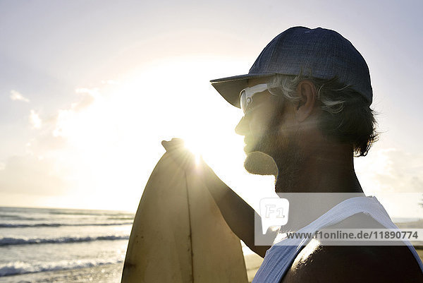 Mann mit Surfbrett beim Sonnenuntergang am Strand