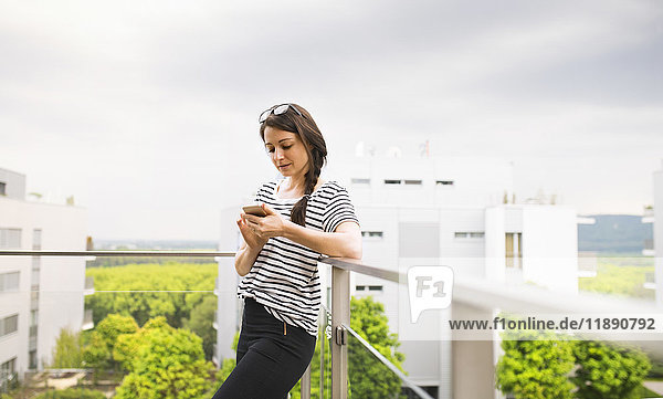 Frau mit Smartphone auf dem Balkon