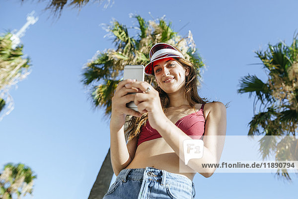 Junge Frau mit Sonnenblende und Bikini per Handy