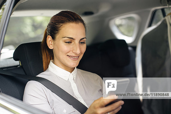 Geschäftsfrau sitzt auf dem Rücksitz eines Autos und schaut auf das Handy.