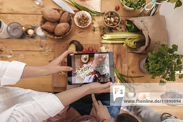 Friends cooking together taking picture of prepared vegetables with tablet  top view