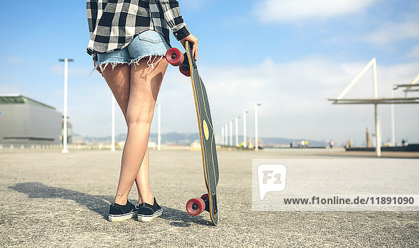 Rückansicht der jungen Frau mit Longboard vor der Strandpromenade  Teilansicht