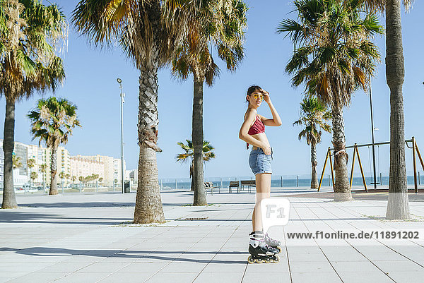 Junge Frau auf Inline-Skates auf einer Strandpromenade mit Palmen