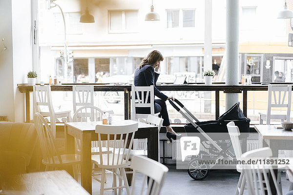 Geschäftsfrau arbeitet vom Café aus mit Kinderwagen an ihrer Seite