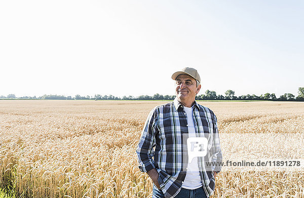 Relaxed senior farmer standing in front of wheat field