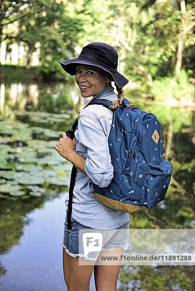 Portrait of smiling woman with backpack standing in front of a lake