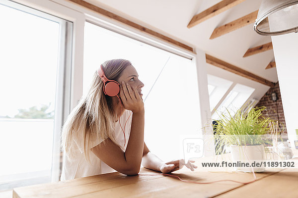 Junge Frau hört Musik mit Kopfhörern  die an Topfpflanzen angeschlossen sind.