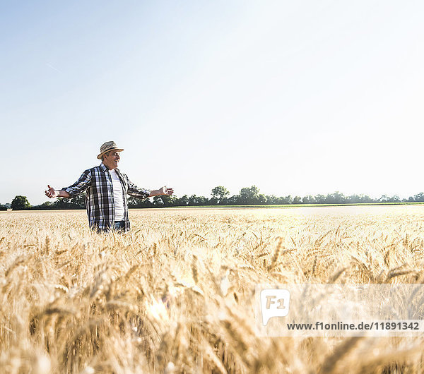 Happy senior farmer standing in wheat field