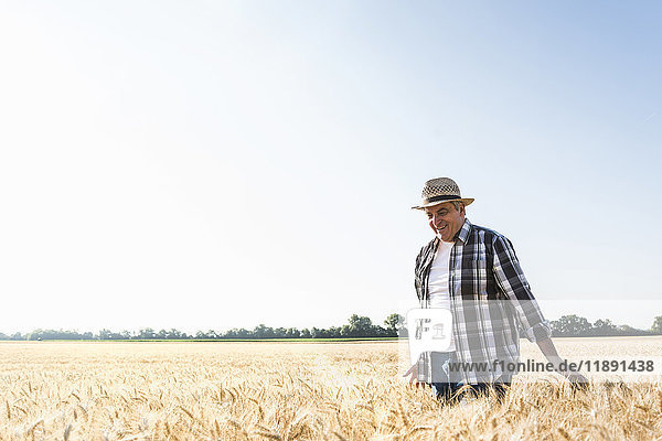 Glücklicher älterer Landwirt  der im Weizenfeld spazieren geht.