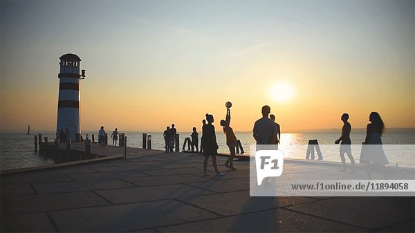 Silhouette of People Playing with Ball on Pier at Sunset