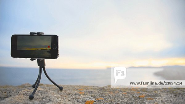 Mobiltelefon auf kleinem Stativ  Videoaufnahme einer Meereslandschaft bei Sonnenuntergang