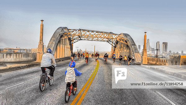 Rückansicht einer Gruppe von Radfahrern  die bei Sonnenaufgang die Brücke überqueren