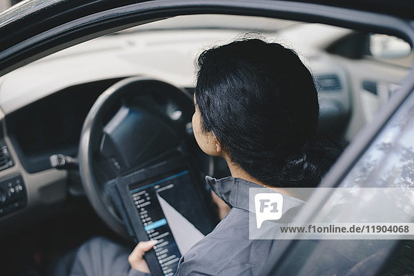 Mechanikerin beim Sitzen im Auto mit digitalem Tablett