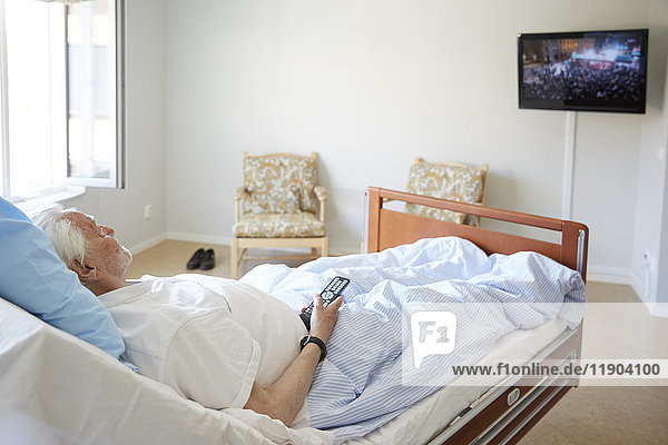 Senior man watching TV while reclining on bed in hospital ward