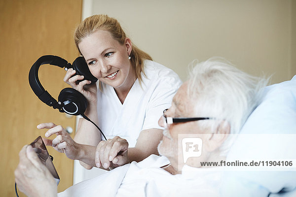 Lächelnde Krankenschwester  die über Kopfhörer Musik hört  während sie ein digitales Tablett auf der Krankenstation benutzt.
