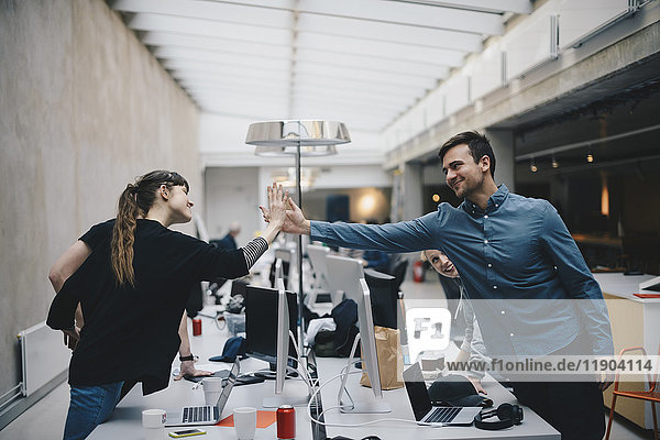 Male and female computer programmers giving high-five over desk in office