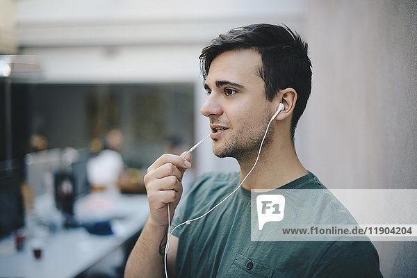 Junger männlicher Programmierer mit In-Ear-Kopfhörer beim Sprechen im Büro