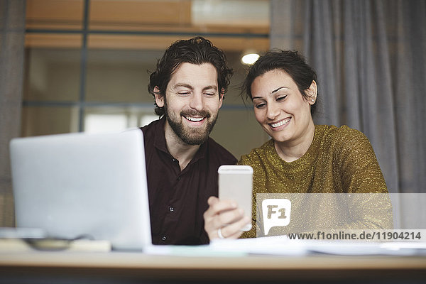 Smiling business colleagues using mobile phone at creative office