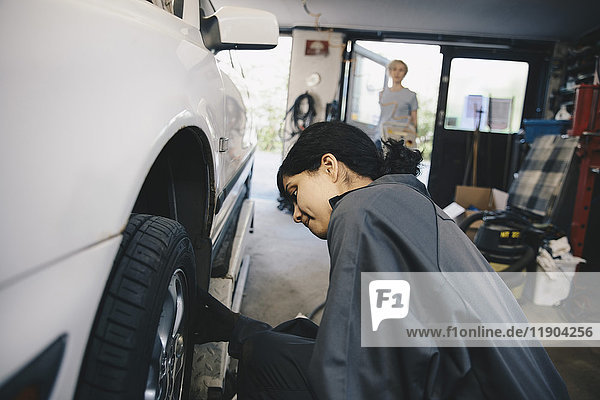Female mechanic examining car wheel at auto repair shop
