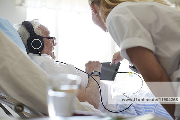Side view of female nurse assisting senior man in using digital tablet on hospital bed