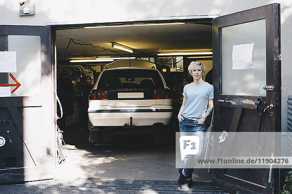 Porträt einer selbstbewussten Frau  die sich an der Tür am Eingang der Autowerkstatt anlehnt.