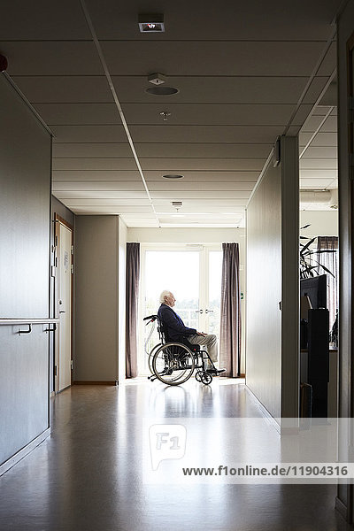 Seitenansicht eines älteren männlichen Patienten  der im Rollstuhl auf dem Flur des Krankenhauses sitzt.