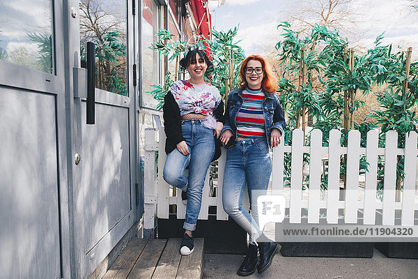 Porträt von Hipster-Freundinnen  die am Zaun stehen.