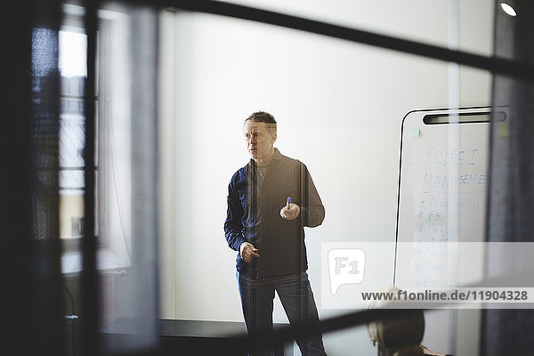 Businessman standing against white wall in board room seen from glass at creative office