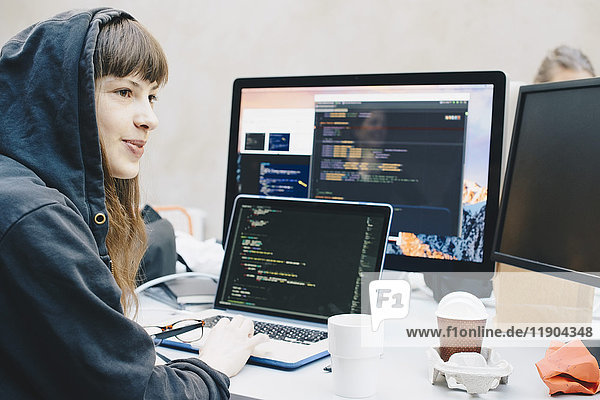 Side view of female computer programmer looking away while using laptop at desk in office