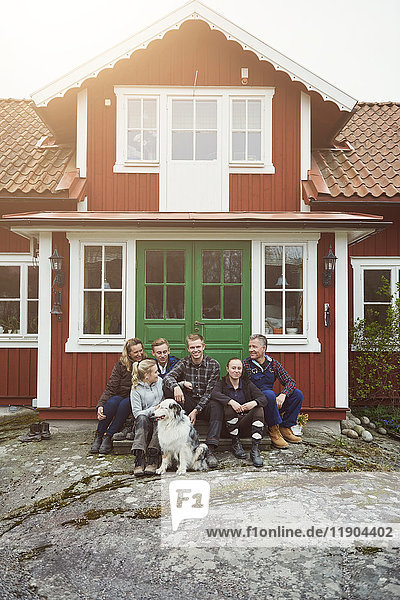 Lächelnde Familie sitzend mit Haustier am Hauseingang