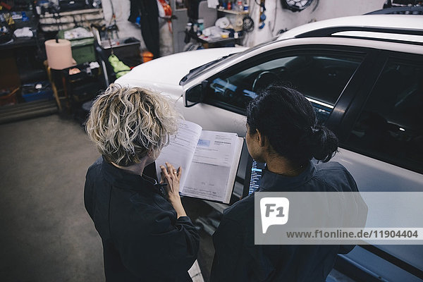 Female mechanic explaining coworker over diary in auto repair shop