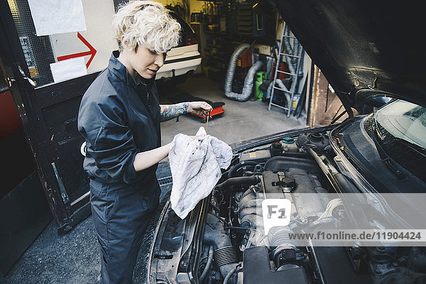 Side view of female mechanic checking oil with dipstick outside auto repair shop