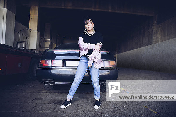 Porträt einer jungen Frau  die auf dem Parkplatz gegen das Auto steht