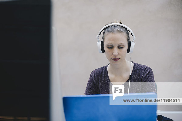 Weibliche Programmiererin mit Kopfhörer bei der Benutzung des Laptops im Büro