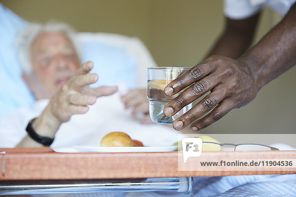 Abgeschnittenes Bild des Krankenpflegers  der dem älteren Mann auf der Krankenstation Trinkglas gibt