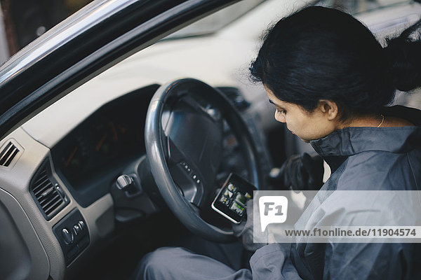 Female mechanic using mobile phone while sitting in car