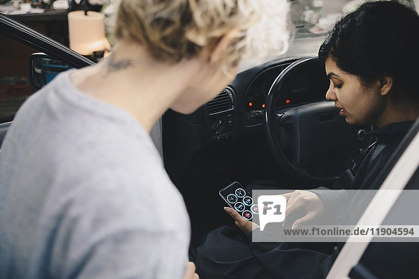 Mechanic explaining application to customer on smart phone while sitting in car