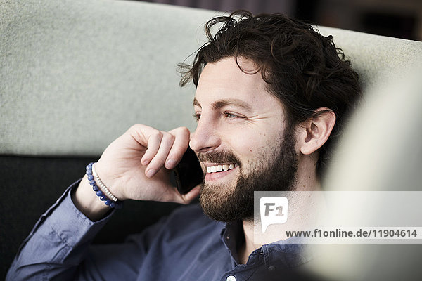 Smiling businessman talking through smart phone while sitting on chair at creative office