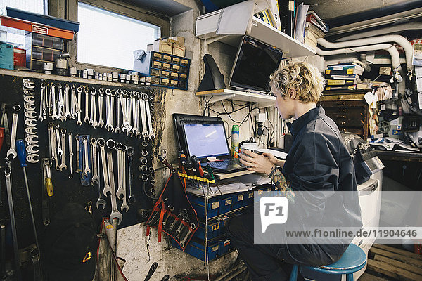 Seitenansicht der Mechanikerin  die den Einwegbecher hält  während sie den Laptop in der Werkstatt benutzt.