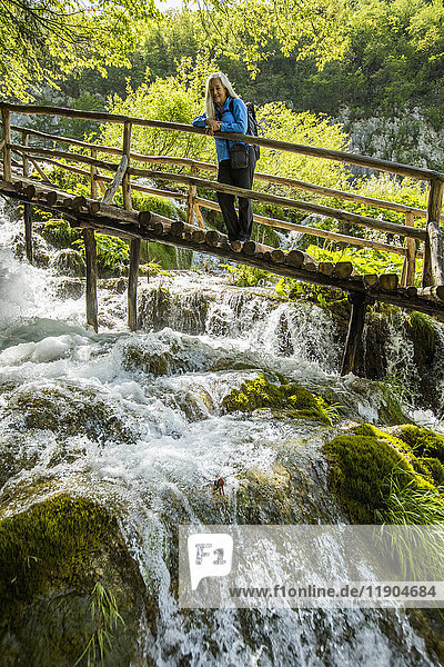 Ältere kaukasische Frau auf Holzsteg bewundert Wasserfall