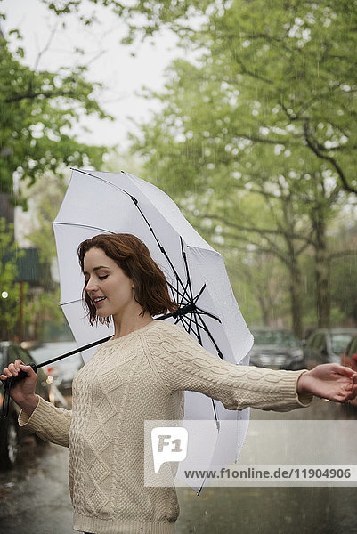 Unbekümmerte kaukasische Frau hält einen Regenschirm im Regen