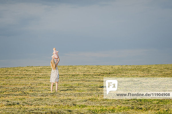 Mutter hebt ihre kleine Tochter auf einem Feld hoch