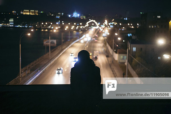 Silhouette einer Person  die den Verkehr von einer nächtlichen Überführung aus beobachtet