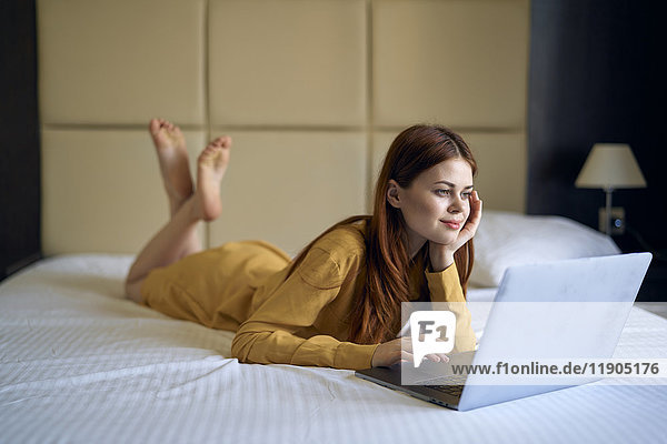 Kaukasische Frau liegt auf dem Bett und benutzt einen Laptop