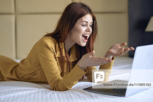 Aufgeregte kaukasische Frau auf dem Bett liegend mit Laptop