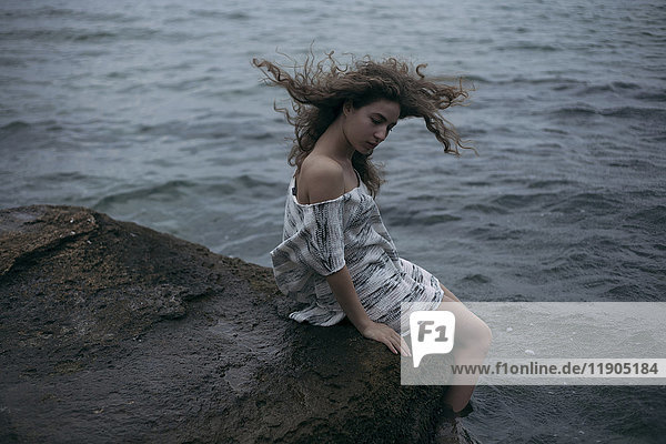 Wind weht Haare der kaukasischen Mädchen sitzen am Meer