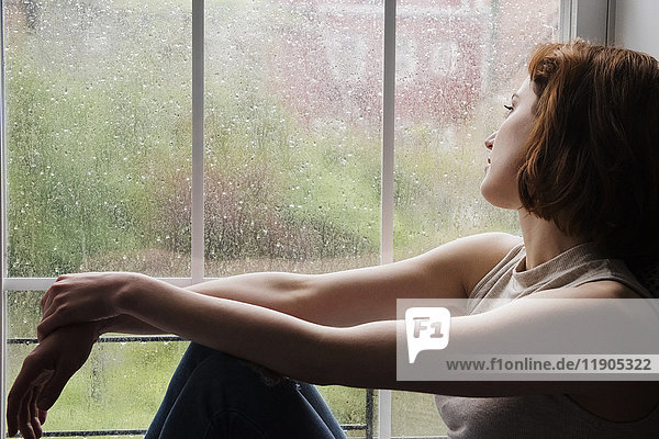 Kaukasische Frau sitzt in der Nähe von regnerischen Fenster Tagträumen