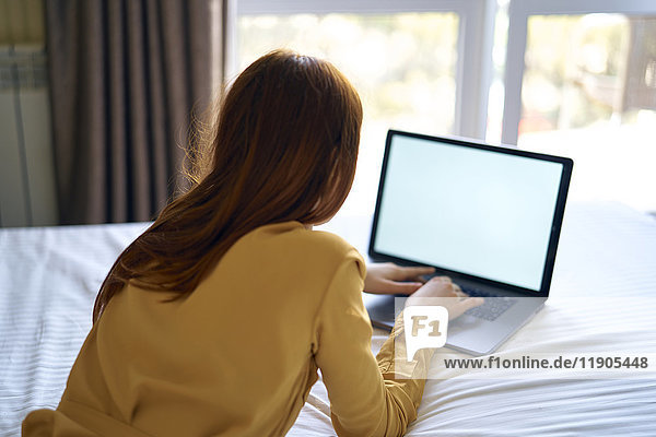 Kaukasische Frau liegt auf dem Bett und benutzt einen Laptop