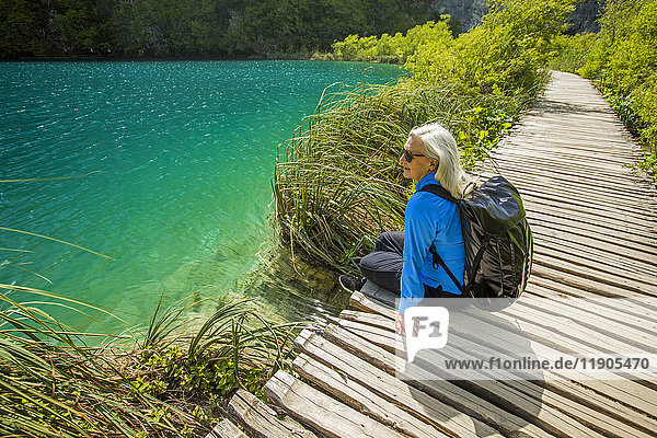 Ältere kaukasische Frau sitzt auf einem Holzsteg in der Nähe von Wasser