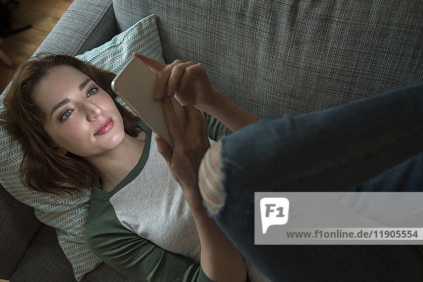 Kaukasische Frau liegt auf dem Sofa und schreibt eine SMS auf ihrem Handy